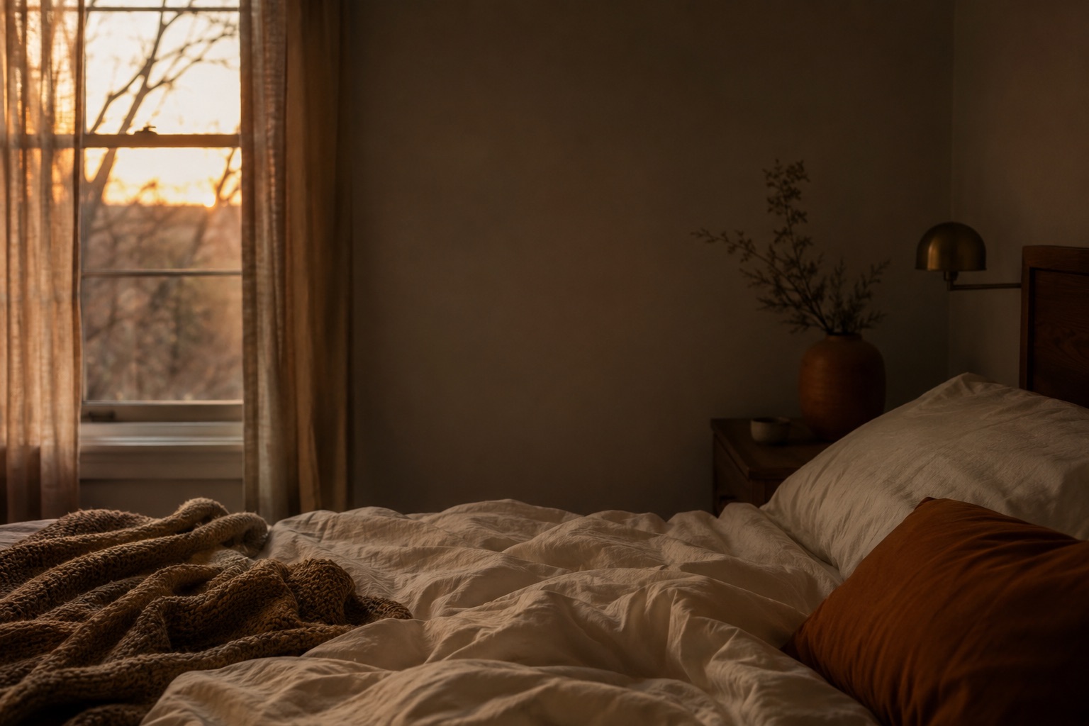 Dark bedroom at dawn with rumpled bedding and soft light through curtains