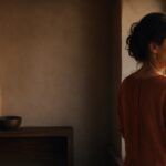 Woman standing by a window in warm evening light, looking away