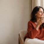 Woman in a terracotta jumper sitting by a window holding a warm drink