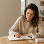 Woman writing in a symptom-tracking journal while tapering off HRT at her kitchen table