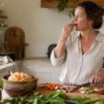 Woman chopping colourful vegetables beside a bowl of fermented food, tasting a piece