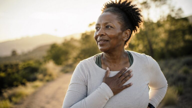 Woman outdoors after a jog resting a hand on her chest to catch her breath