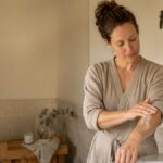 Woman applying body lotion along her forearm in warm bathroom light