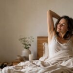 Woman waking and stretching her arms in bed in warm morning light