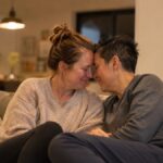 A couple sitting close on a sofa with foreheads gently touching in soft evening light