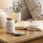 Magnesium supplement bottle and a glass of water on a bedside table in the evening